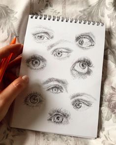 a hand holding a pen over a notebook with eye drawings on it