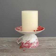 a white candle sitting on top of a red and white bowl filled with raspberries