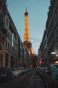 the eiffel tower is lit up at night, with cars parked in front