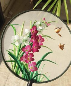 a mirror with flowers painted on it and butterflies in the air next to plants that look like they are flying