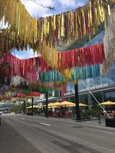 colorful streamers hanging from the side of a building next to a sidewalk with tables and umbrellas