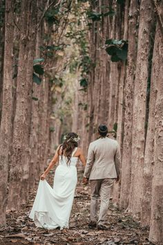 a bride and groom walking through the woods holding each other's hands as they walk