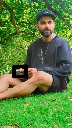 a man sitting on the grass with his laptop in front of him and trees behind him