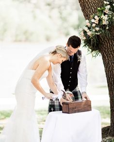 a bride and groom are cutting their wedding cake at the table outside under a tree