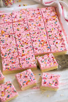 pink frosted cake squares with sprinkles on a white tray next to a spoon