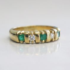 This stunning 18K yellow gold ring features two very white round brilliant cut diamonds and three bright green round emeralds. This ring is perfect for an anniversary band, wedding band, or stackable ring. The contrast of the colors makes sure this ring stands out! Metal: 18K Yellow Gold Diamonds: .20 CTW, VS1-VS2, E-F Color Emeralds: 3 MM Each Band Width: 3.44 - 5.00 MM Size: 7 For a greater selection of jewelry please visit our website at www.BlackMarketLLC.com If you have any questions about Classic Green Emerald Ring With Single Cut Diamonds, Classic Green Rings With Single Cut Diamonds, Classic Green Diamond Ring With Single Cut Diamonds, Green Round Diamond Ring With Channel Set, Green Diamond Half Eternity Ring For Anniversary, Green Diamond Ring For Anniversary With Half Eternity Band, Green Emerald Ring With Single Cut Diamonds For Promise, Green Diamond Ring With Single Cut Diamonds For Anniversary, Emerald Green Promise Ring With Single Cut Diamonds