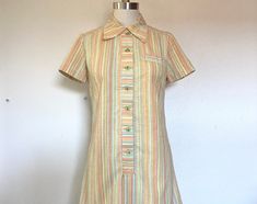 "Cute mini dress in textured, yarn dyed striped cotton in orange, green, yellow, blue, brown and white.  -pointed Peter Pan collar -green buttons up the front -a-line shape -faux chest pocket Size Small  Measures  36.5\" around the bust  33.5\" around the waist  39\" around the hips  33\" long from shoulder to hem  Label- none Fabric- cotton Condition- wonderful, no flaws to note" Striped Collared Mini Dress For Summer, Collared Striped Mini Dress For Spring, Green Cotton Mini Dress For Work, Summer Button-up Dress With Striped Collar, Retro Collared Mini Dress For Summer, Retro Collared Mini Dress For Spring, Fitted Multicolor Mini Dress With Buttons, Retro Mini Dress With Button Closure For Spring, Vintage Button-up Mini Dress