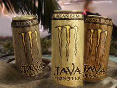 three monster energy drink cans sitting on top of a sandy beach next to a palm tree