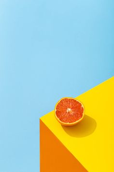 an orange slice sitting on top of a yellow and blue block against a blue sky