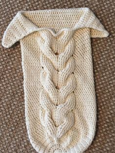 a crocheted sweater with a knot on the front and back end, laying on top of a brown carpet