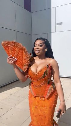 a woman in an orange dress is holding a fan