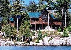 a log cabin sits on the shore of a lake surrounded by pine trees and rocks