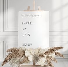 an easel with some flowers on it in front of a sign that says welcome to the wedding of rachel and john