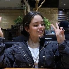 a woman sitting at a table with her hands up in the air while making peace signs