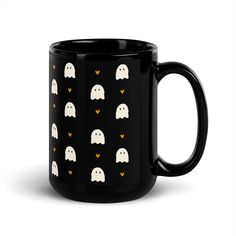 a black mug with white ghost faces on it and hearts in the shape of ghosts