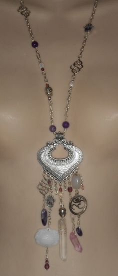 "This handcrafted bohemian, hippie, boho necklace has been created from amethyst stone beads, wire wrapped crystal points, hamsa charms, spiritial head charm beads, an OHM charm with a tiny amethyst inset stone and a carved glass lotus pendant.  The overall length from lobster clasp closure to bottom of crystal point measures 19 1/2\". The antique silver tone metal pendant along measures 2 1/4\" wide and 2 1/4\" tall." Wrapped Crystal Point, Crystal Amethyst, Lotus Pendant, Hamsa Charm, Chevron Necklace, Surfer Style, Witch Jewelry, Wire Wrapping Crystals, Triangle Necklace