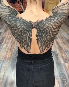 the back of a woman's body with wings on her shoulder and chest, in front of a brick wall