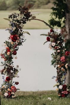 an outdoor wedding arch decorated with flowers and greenery by the water's edge