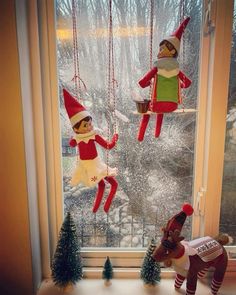 two elfs are hanging from the windowsill