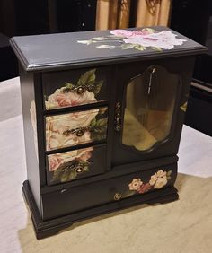 an ornate black cabinet with flowers painted on it's doors and drawers, sitting on a table