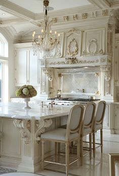 an ornate kitchen with white cabinets and marble counter tops, chandelier above the island