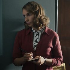 a woman holding a pen and writing on a piece of paper in front of a mirror