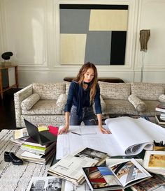 a woman sitting on top of a couch surrounded by books and papers in a living room