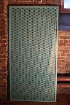 a green metal screen sitting on top of a wooden floor next to a brick wall