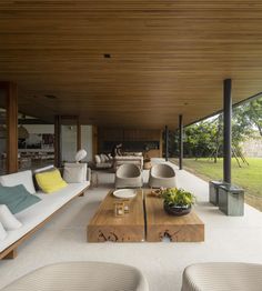 a living room filled with furniture under a wooden roof next to a lush green field