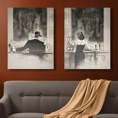 two black and white paintings hang on the wall next to a couch with a blanket draped over it