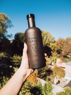 a hand holding up a black bottle with the words tribe spirit on it and trees in the background