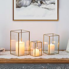 three lit candles sitting on top of a table in front of a framed photo and an empty vase