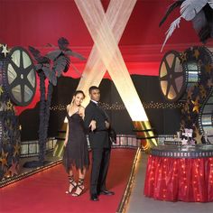 a man and woman standing on a red carpet in front of a stage with lights