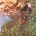 a woman in a white dress taking a photo with her cell phone while standing in a field