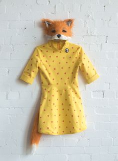 a stuffed fox head hanging on the wall next to a yellow dress with polka dots