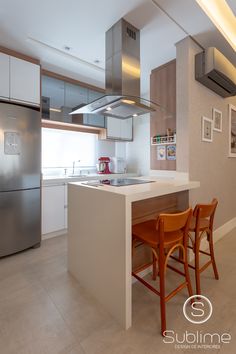 a modern kitchen with stainless steel appliances and white counter tops, along with two wooden bar stools