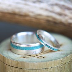 two wedding rings sitting on top of a piece of wood with blue glitter in the middle