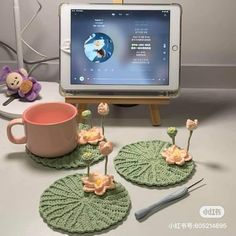 there are three crocheted coasters with flowers and a cup on the table