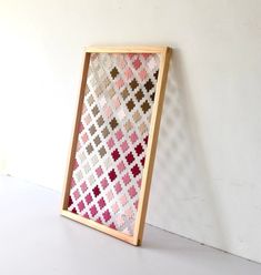 a wooden frame with a pink and brown cross - stitch pattern on the front is leaning against a white wall