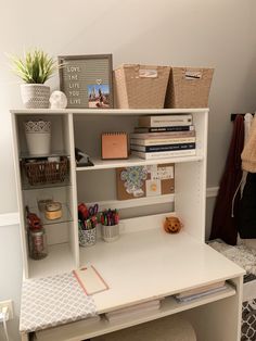 a white desk topped with lots of books and other office supplies next to a wall