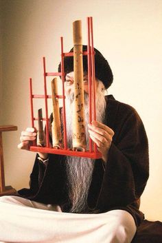 an old man with long white hair and beard holding up a wooden structure made out of bamboo sticks