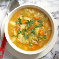 a bowl of soup with carrots, potatoes and parsley in it on a marble table