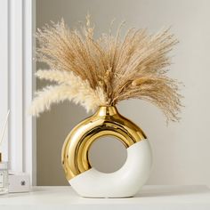 a gold and white vase with some dry grass in it