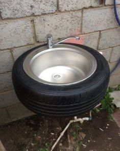 an old tire turned into a sink in front of a brick wall with grass growing on the ground