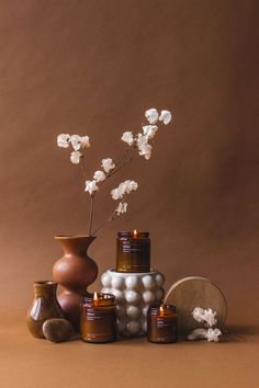 an arrangement of vases and jars with flowers in them on a brown background,