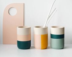 three different colored vases sitting next to each other on a white counter top, one with two straws in it