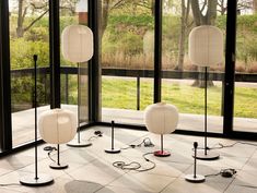 three lamps sitting on top of a tiled floor in front of large glass windows with trees outside