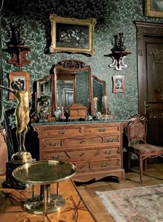 an old fashioned bedroom with green wallpaper and antique furniture, including a mirror on the dresser