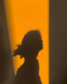 the shadow of a person standing in front of a yellow wall holding a cell phone