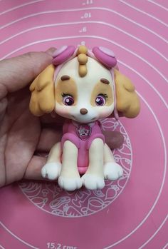 a small toy dog sitting on top of a pink table next to a person's hand